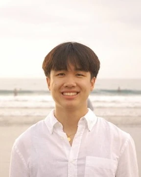 Alexander Chin in a white shirt, smiling on a beach with the ocean in the background.